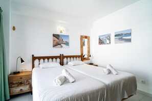 A hotel room with two beds, a wooden headboard, a nightstand with a lamp, a mirror, and artwork on the walls.