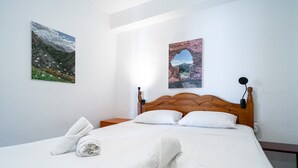 Een net opgemaakt bed met witte lakens en handdoeken, een houten hoofdbord, en twee wandlampen.