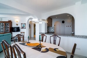 A dining area with a table set for four, surrounded by wooden chairs, a modern pendant light, and a view into the kitchen area.