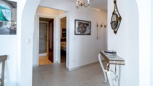 A hallway with a chandelier, a framed map, a mirror, and a small table with a bowl.