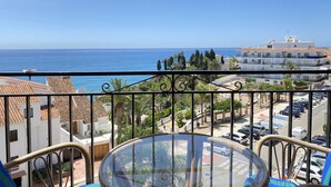 Un balcon offrant une vue dégagée sur la mer, un espace de stationnement et des bâtiments aux toits recouverts de tuiles.