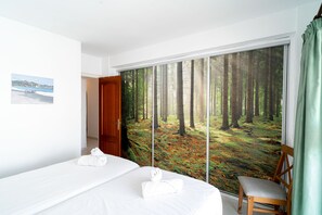 A hotel room with a large window, a bed, a chair, and a painting on the wall.
