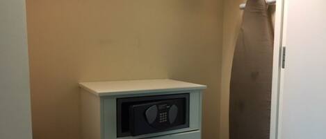 Una habitación compacta con un microondas sobre un mueble pequeño, un perchero y un espejo grande.