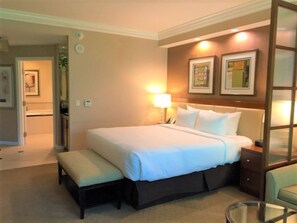 A hotel room with a large bed, bedside tables, a bench, and a glass table.