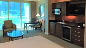 Ein Hotelzimmer mit einem großen Bett, einem Essbereich mit Tisch und Stühlen, einer Küchenzeile mit Mikrowelle und Backofen sowie einem Fernseher, der über dem Tresen angebracht ist.
