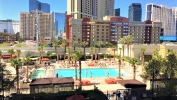 Ein Hotel mit Poolbereich, umgeben von Palmen und modernen Gebäuden im Hintergrund.