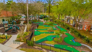 A golf course with a putting green, a children's play area, and surrounding trees.