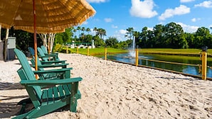 Une plage avec des chaises Adirondack vertes, un parasol en paille et un élément décoratif aquatique.