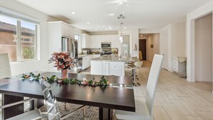 A modern kitchen with white cabinets, a central island, and a dining area with a dark table and chairs. - Luxury Golf Retreat w/ Saltwater Pool, Spa &  View, Walk2-Coachella, Stagecoach (Indio)