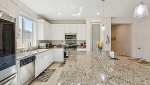 A modern kitchen with white cabinets, granite countertops, stainless steel appliances, and a central island. - Luxury Golf Retreat w/ Saltwater Pool, Spa &  View, Walk2-Coachella, Stagecoach (Indio)