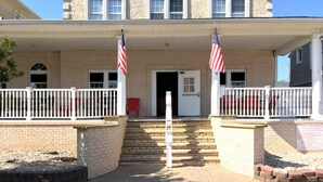 A two-story building with a covered front porch, two American flags, and a red chair. - Half Block from Belmar Beach!! (Belmar)