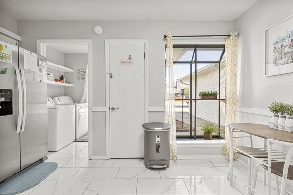 A modern kitchen with white appliances, a trash bin, and a dining area with a table and chairs.