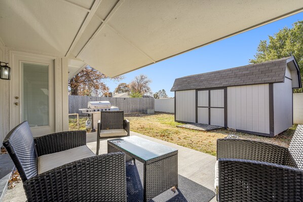 A covered patio with wicker furniture, a barbecue grill, and a shed.