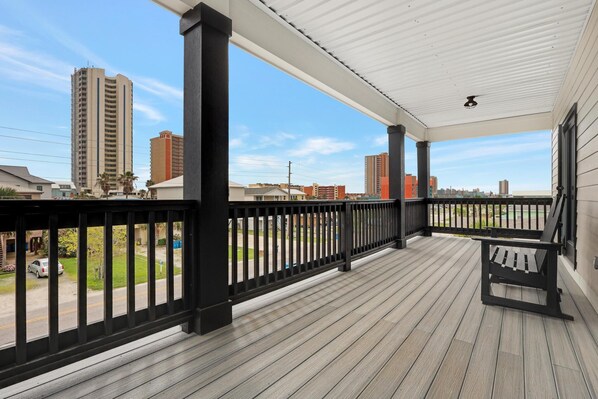 A covered outdoor area with a wooden deck, black railings, and a bench.