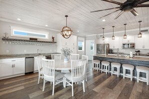 A modern kitchen with white cabinetry, a central island with stools, and pendant lighting. - Black Pearl - New Spacious Home with Pool-Gulf Shores- Signature Properties (Gulf Shores)