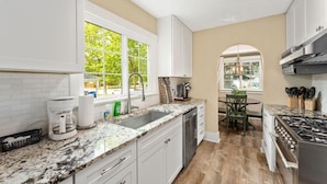 Una cocina moderna con armarios blancos, encimera de granito, estufa integrada y ventana que proporciona luz natural.