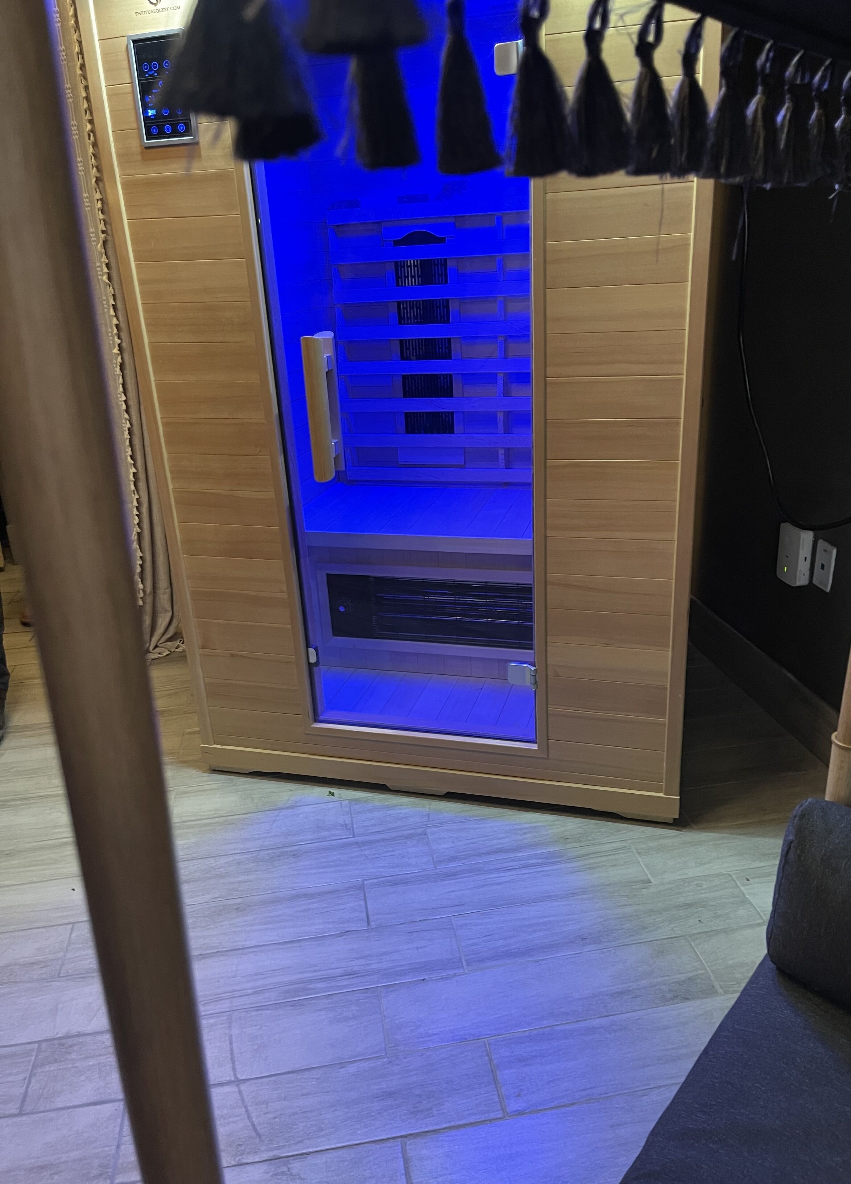 A sauna with a wooden exterior and a glass door, featuring a control panel and a ventilation system.