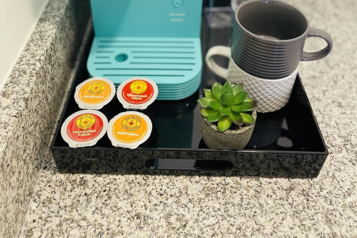 A Keurig coffee maker on a countertop with a black tray holding coffee pods and a small potted plant.