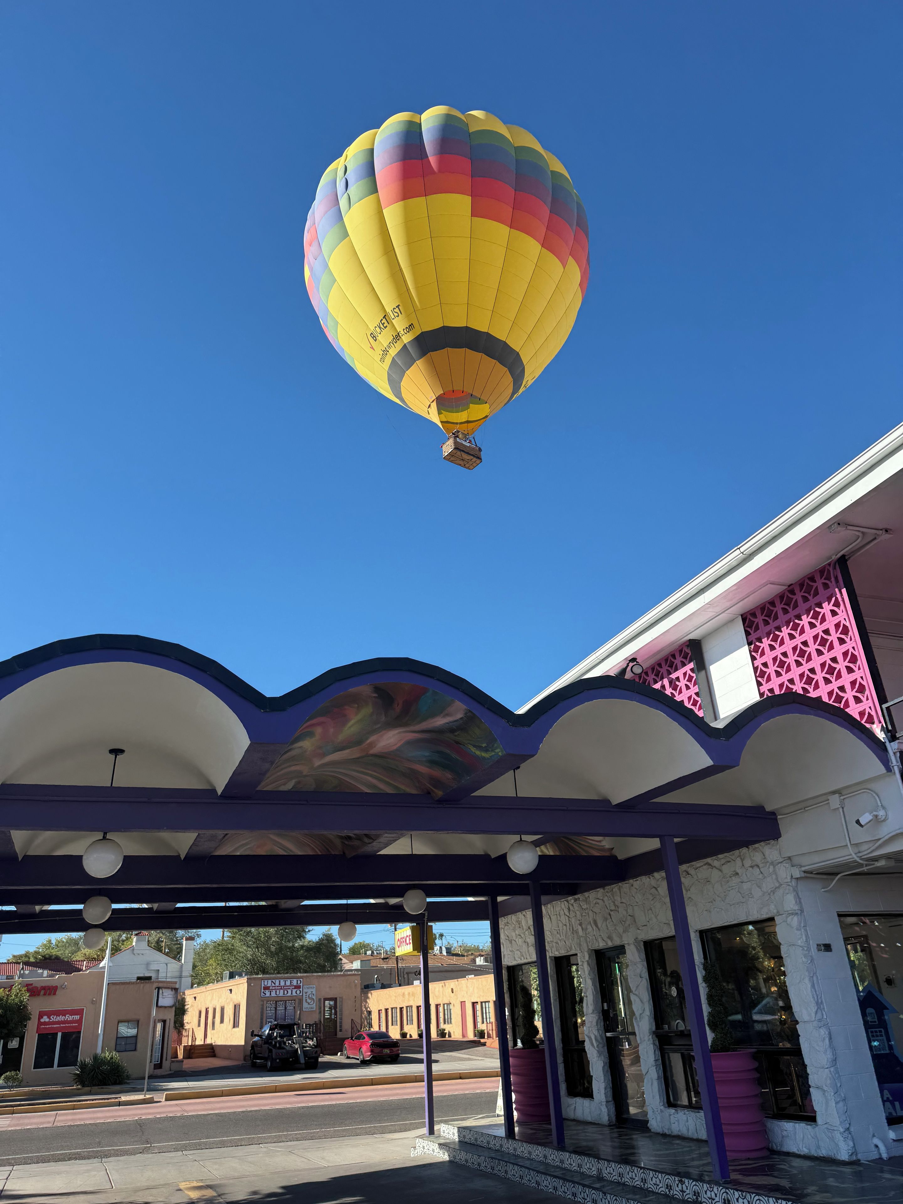 Eine Heißluftballon mit farbenfrohem Muster schwebt über einem Gebäude mit auffälliger rosa-lila Fassade.