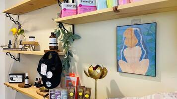 A shelf with various skincare products, a painting, and a small plant.