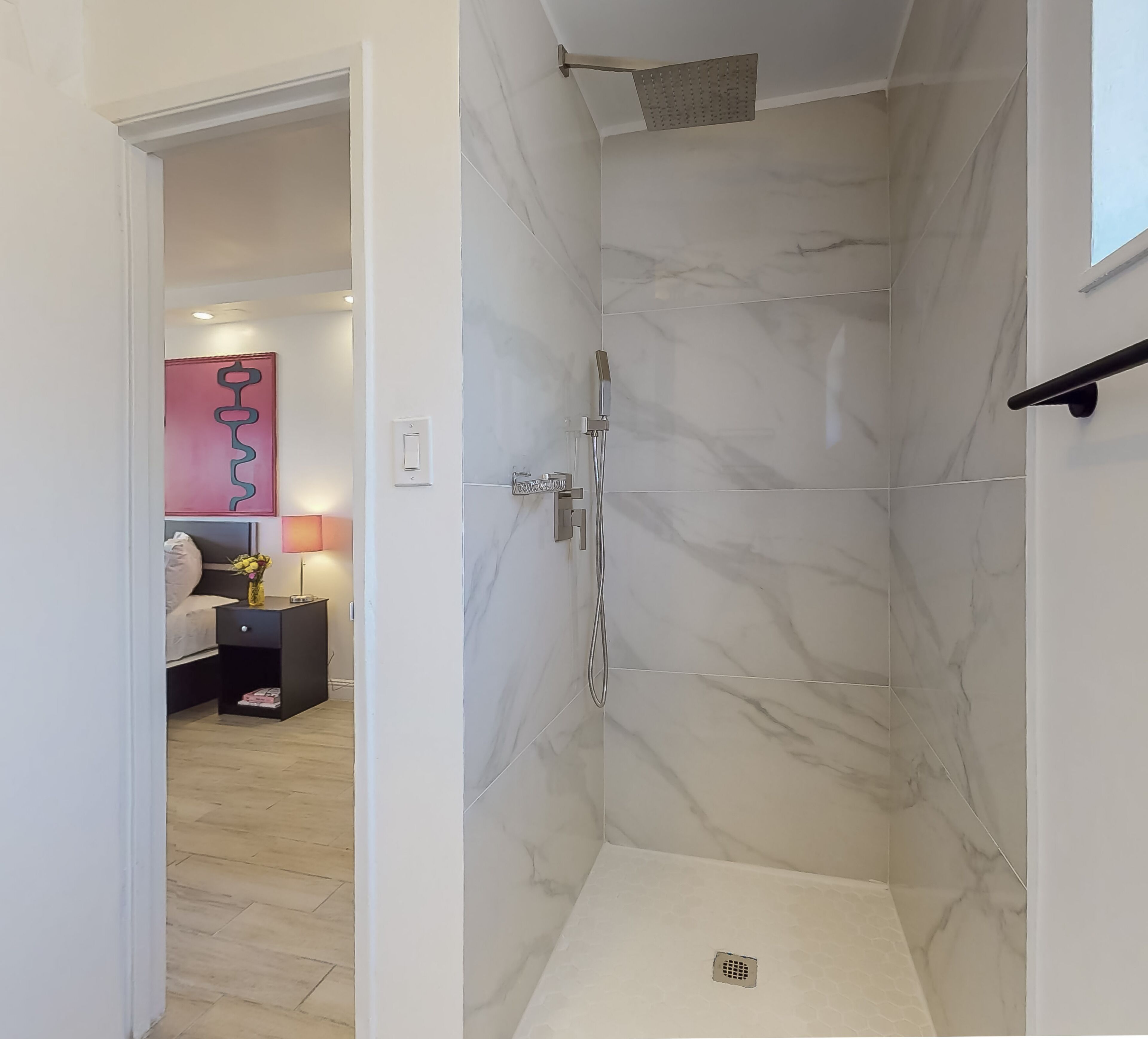 A modern bathroom with a walk-in shower, marble walls, and a visible drain.