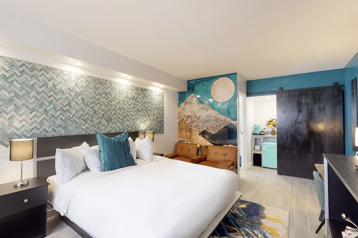 A modern hotel room with a large bed, a sofa, a desk, and a bathroom visible through an open door.
