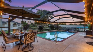 An outdoor pool area with a covered patio, chairs, and string lights. - WALK TO BEACH • Waterfront •Direct Gulf Access •South Facing Heated Pool • 4  Kings (Cape Coral)