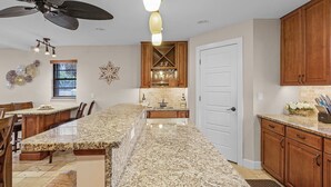 A kitchen with granite countertops, wooden cabinets, a ceiling fan, and a built-in island with seating. - WALK TO BEACH • Waterfront •Direct Gulf Access •South Facing Heated Pool • 4  Kings (Cape Coral)