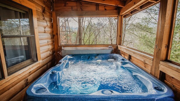 Un bain à remous dans un chalet en bois, avec vue sur les arbres à travers les fenêtres.