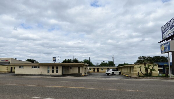 A motel with a parking lot, a white car parked in front, and a billboard advertising women's health services.