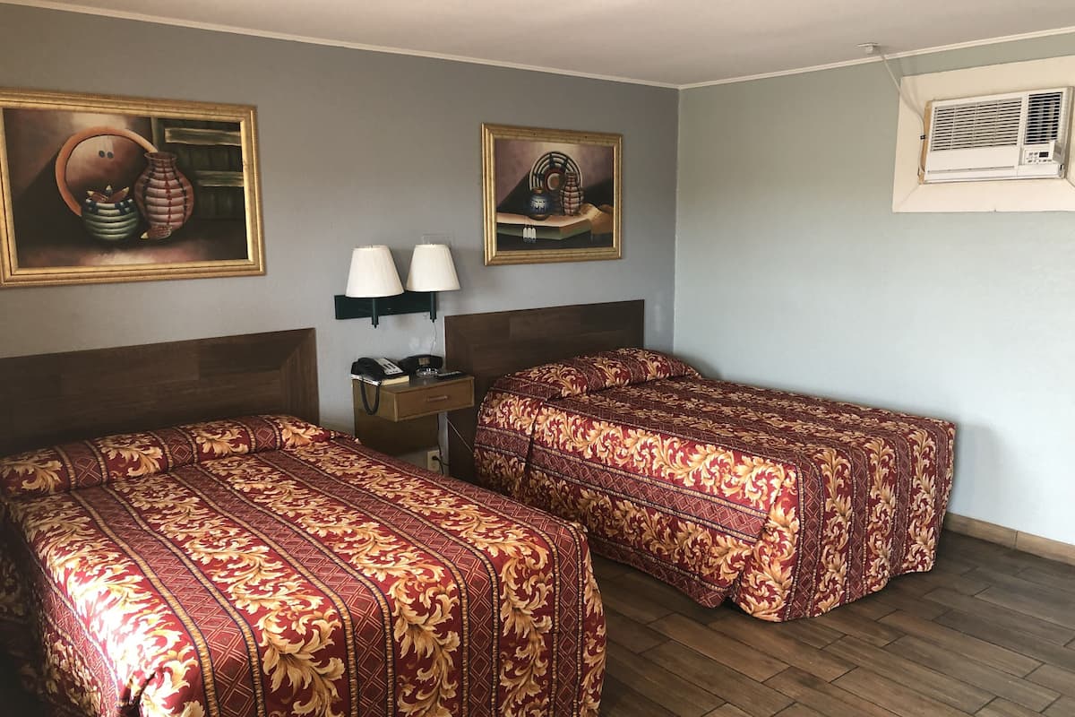 Ein Hotelzimmer mit zwei Betten, einem Nachttisch mit Lampen, einem Telefon und zwei gerahmten Kunstwerken an der Wand.