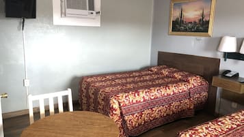 A room with a bed, a desk, a chair, a round table, an air conditioning unit, and a painting on the wall.