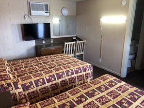 A hotel room with two beds, a desk, a chair, a television, and an air conditioning unit.