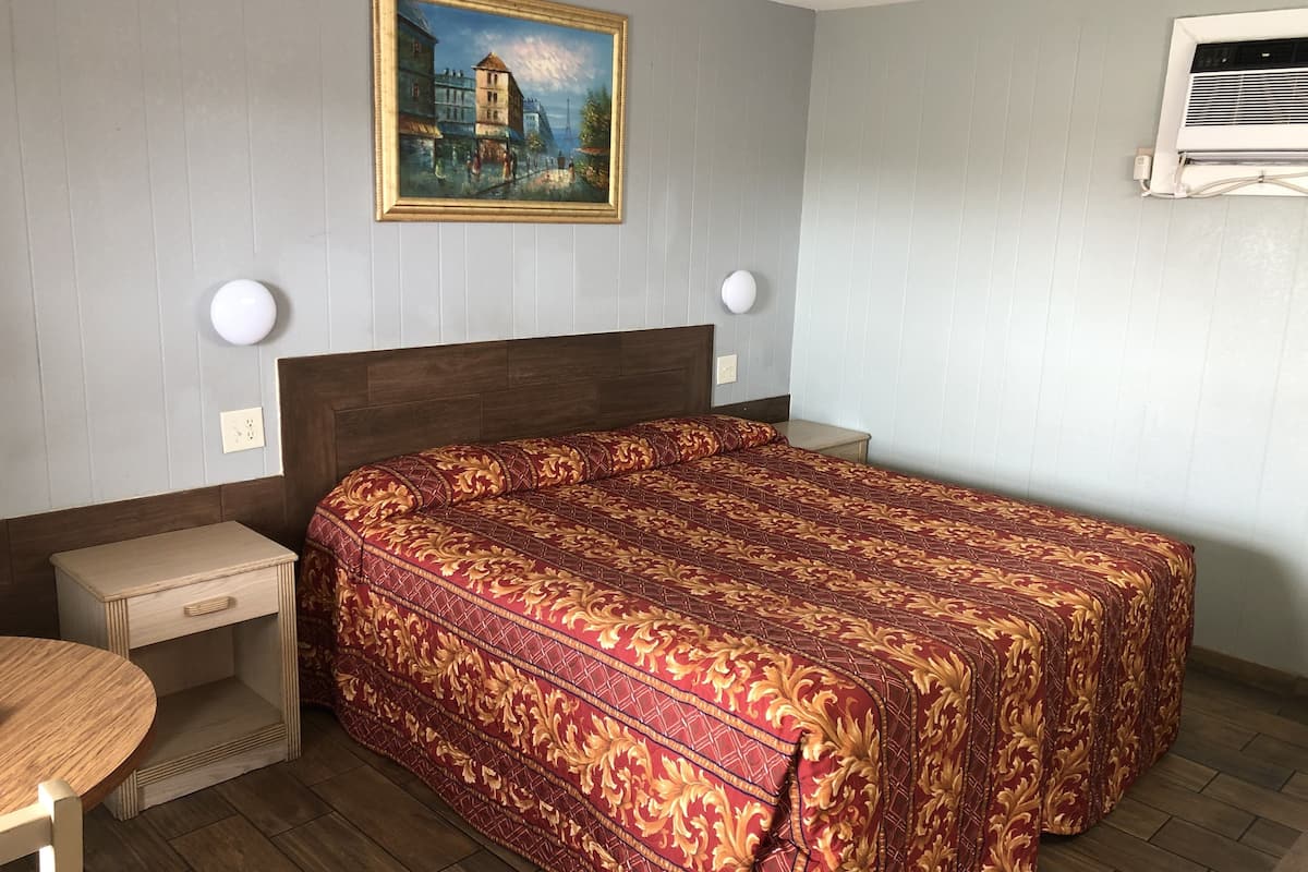 Ein Hotelzimmer mit Bett, Nachttischen, einem Bild an der Wand und einer Klimaanlage.
