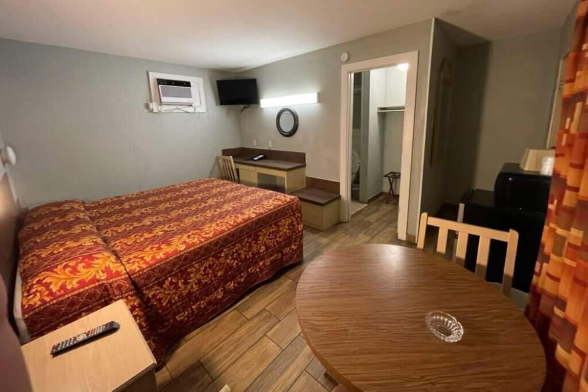 Ein kleines Hotelzimmer mit Bett, Schreibtisch, runder Tisch, Fernseher und Spiegel.