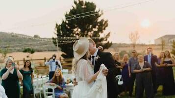 A wedding ceremony with a couple embracing on a blanket, guests seated around them, and a sunset in the background.