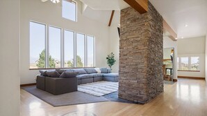A spacious living room with a large sectional sofa, a stone accent wall, and large windows offering a view of the outdoors.