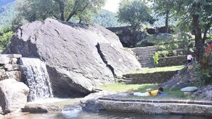 A natural setting with a waterfall, stone steps, and a person lying on a mat by the water. - Swiss Tent 4 (Dharamshala)