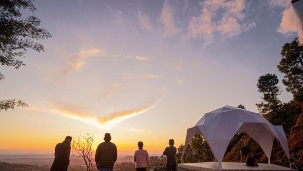 A group of people standing on a hill overlooking a sunset, with a white tent-like structure in the foreground. - Swiss Tent 4 (Dharamshala)