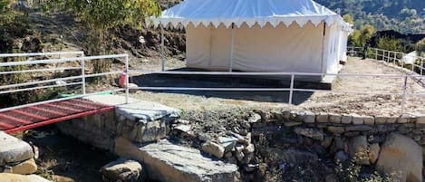 A white tent with a peaked roof, set on a stone platform with a metal railing.