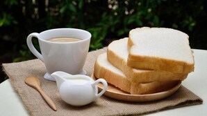 A white cup of coffee, a small white pitcher, and a stack of white bread on a wooden plate, set on a table with a burlap cloth. - Swiss Tent 4 (Dharamshala)