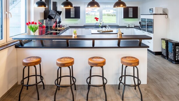 Una cocina moderna con una isla central, taburetes de bar, iluminación colgante y vistas al exterior.