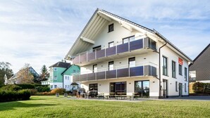 Un edificio moderno con tejado plano, varios balcones y una zona de estar al aire libre techada.