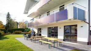 Un edificio moderno con una zona de estar exterior cubierta, paneles solares y vistas del paisaje circundante.