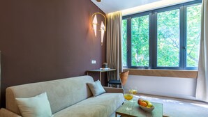 A modern living room with a sofa, a table with fruit and drinks, a window with curtains, and a wall-mounted light fixture. - Bosket Luxury Rooms (Split)