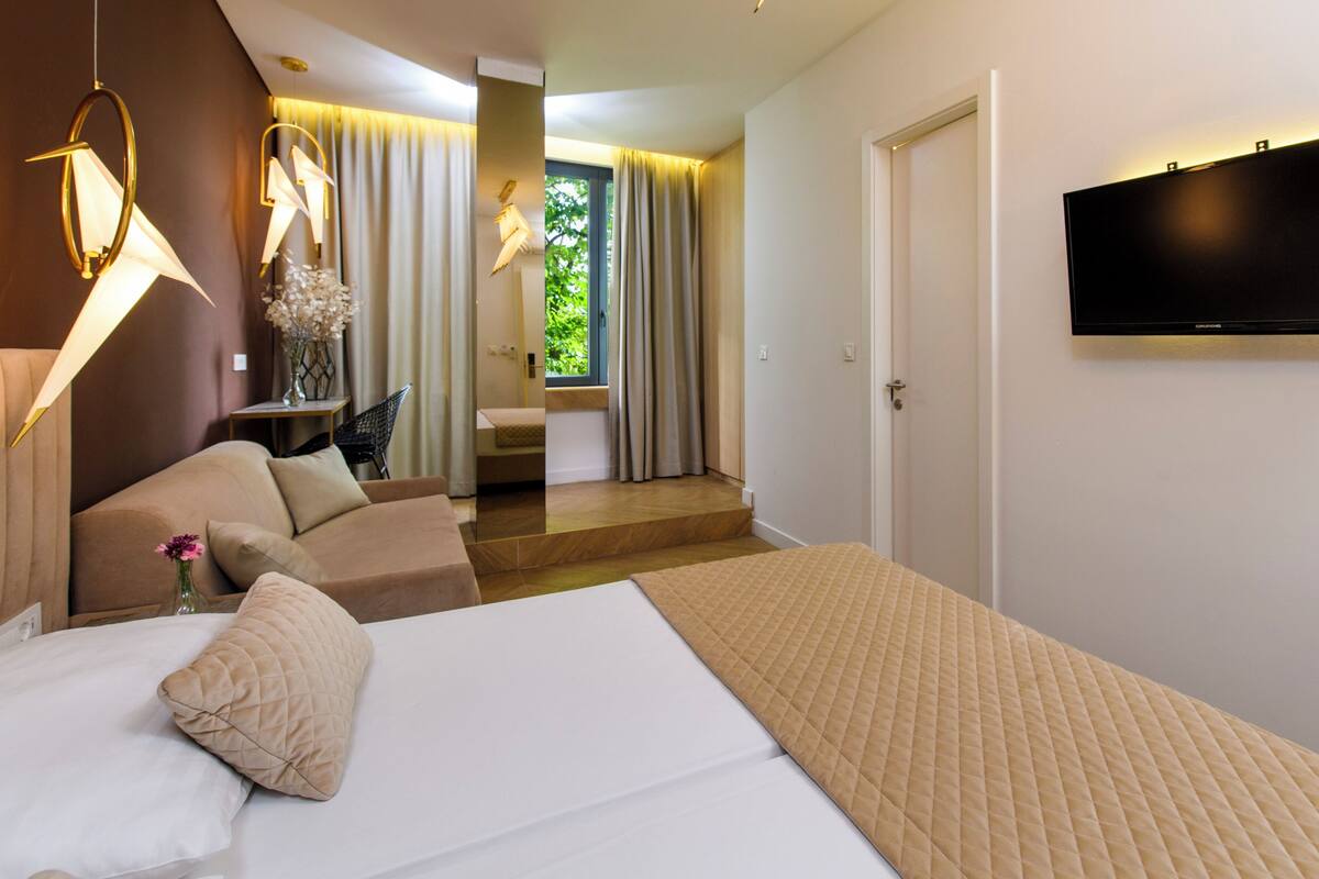 A hotel room with a bed, a sofa, a TV mounted on the wall, and a view of the outside.
