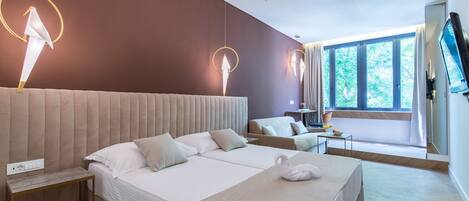 A modern hotel room with a large bed, a sofa, a desk, and a TV.