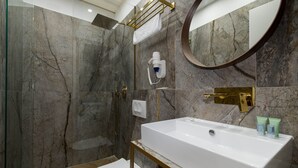 A modern bathroom with a marble shower wall, a white sink with gold fixtures, and a large mirror. - Bosket Luxury Rooms (Split)