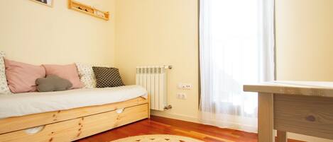 A bedroom with a wooden bed, a round woven rug, a radiator, and a window with sheer curtains.
