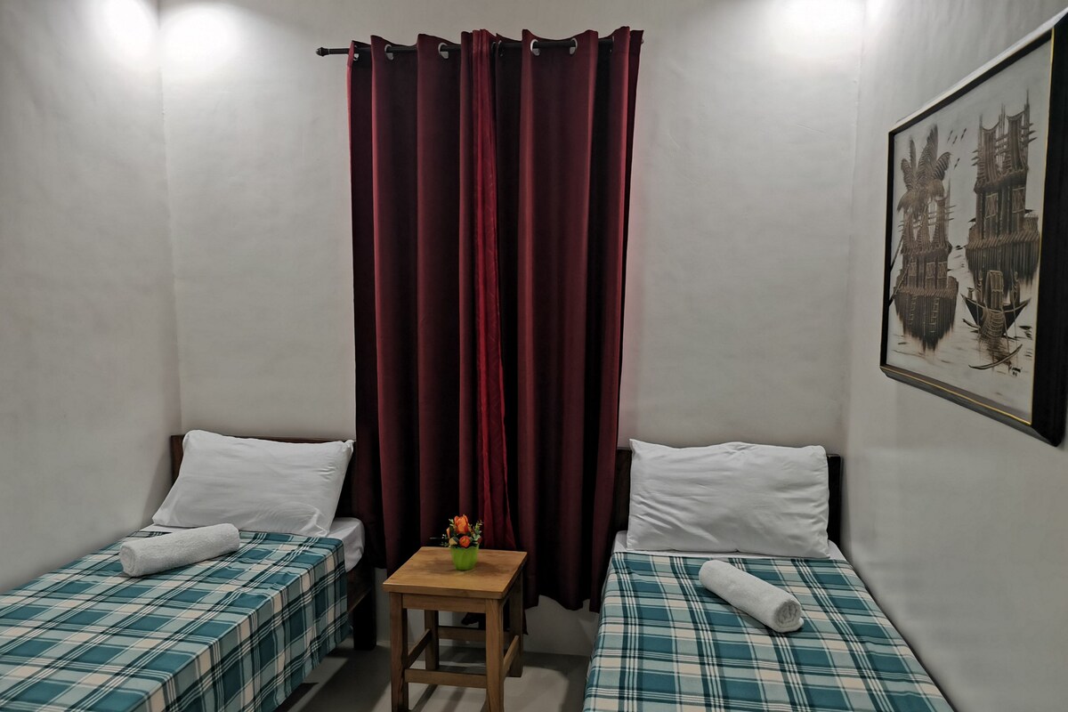 Una habitación con dos camas, una mesita pequeña y una cortina.